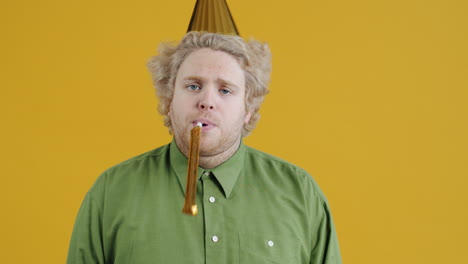 man blowing party horn in front of yellow background