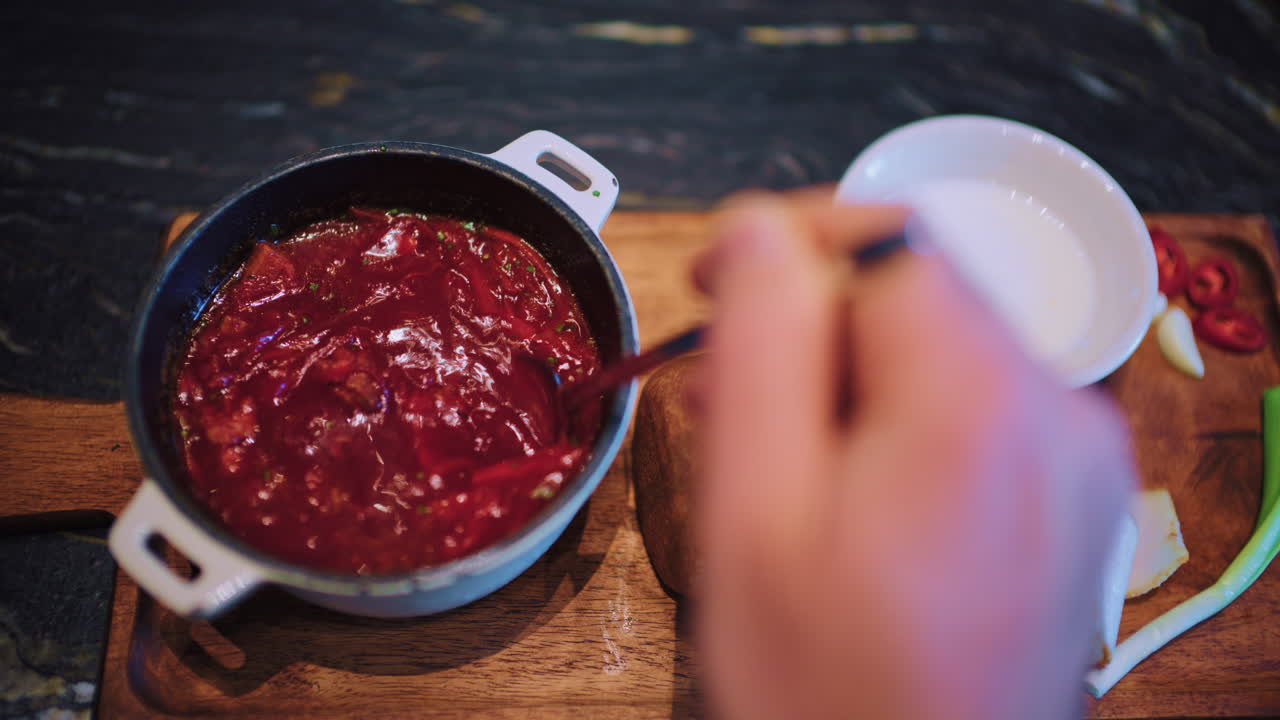 Close up of a spoon stirring borscht inside a small pot placed on a wooden board
