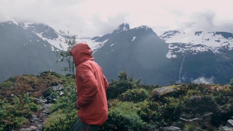 slow motion shot of a man in a jacket running over rocky terrain in the mountains, beautiful snow covered mountains in the background.