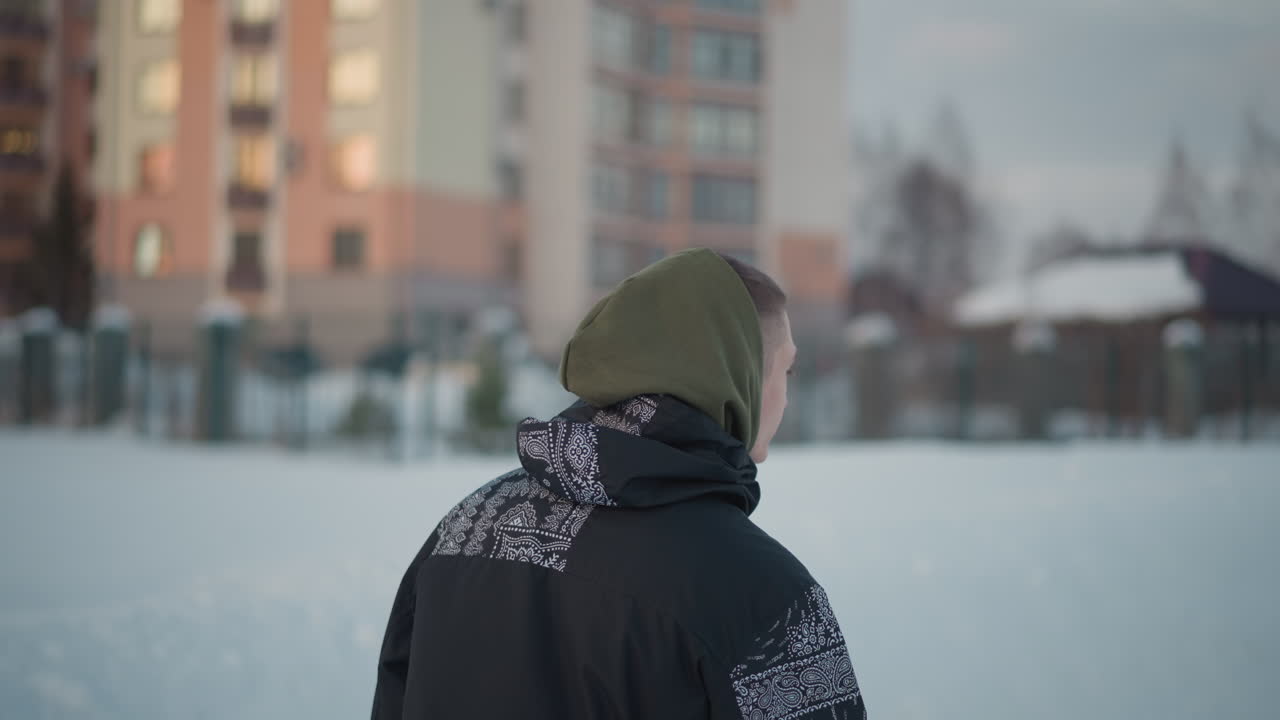back view of teen in hooded jacket gliding on ice surface with blurred winter evening light reflecting off modern building backdrop, serene motion captured in snowy park environment