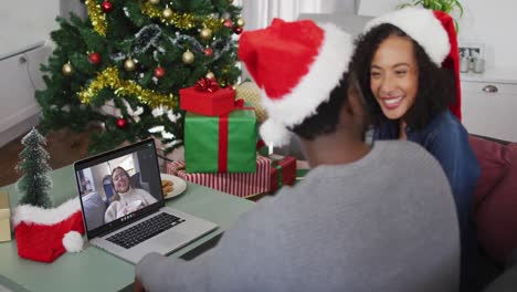 Afroamerikanisches-Paar-Mit-Weihnachtsmützen,-Das-Zu-Weihnachten-Zu-Hause-Einen-Videoanruf-Auf-Dem-Laptop-Führt