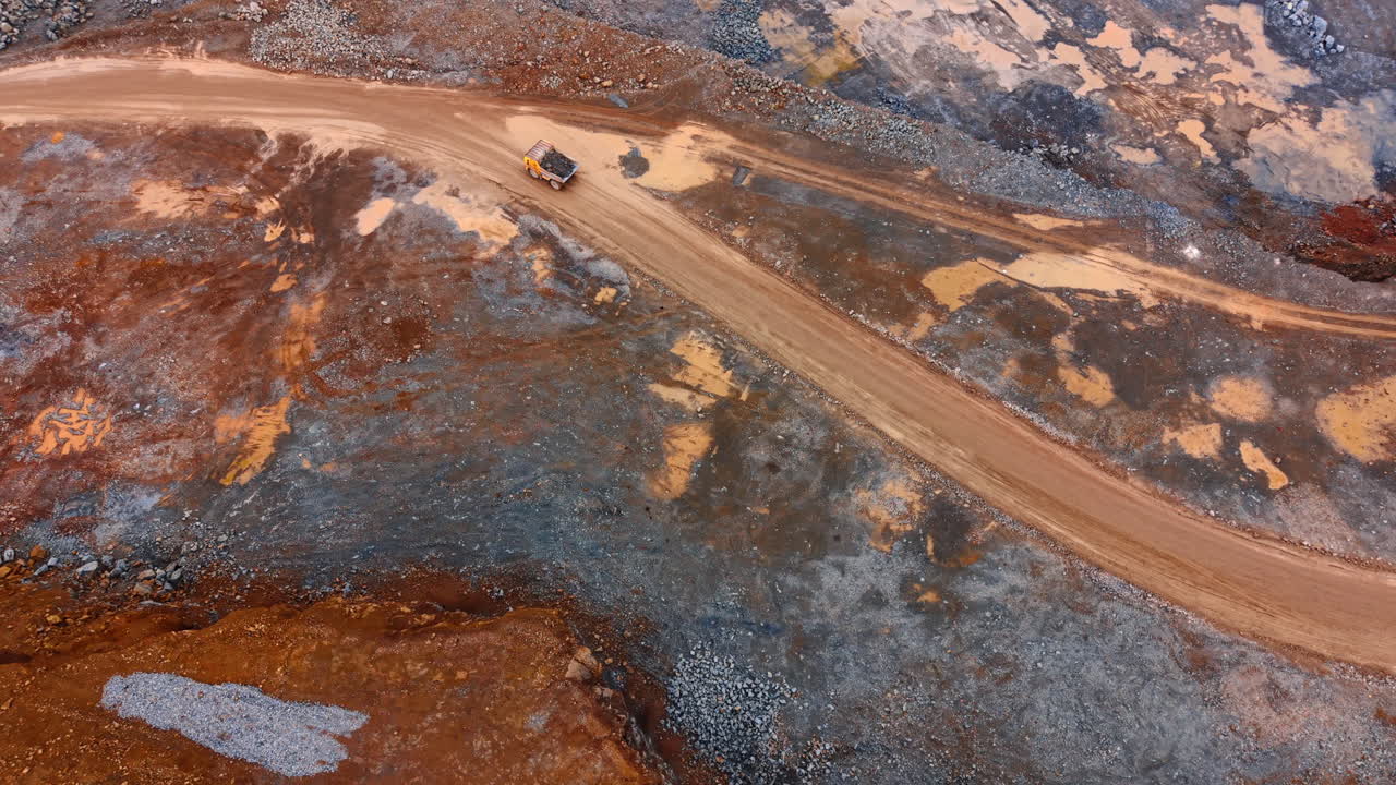 Aerial view of heavy dump truck driving on dirt quarry road. Top down perspective of a mining truck transporting stone across an industrial site with textured ground