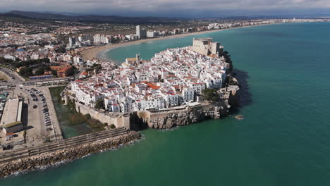 sunny aerial of peniscola’s castle and town jutting into sea with marina to one side