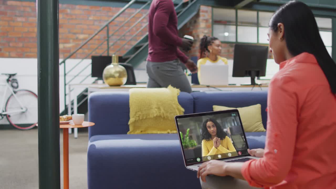 mujer de negocios biracial usando una computadora portátil para una videollamada con un colega de negocios biracial