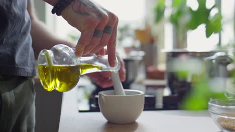 chef pouring olive oil in mortar and using pestle
