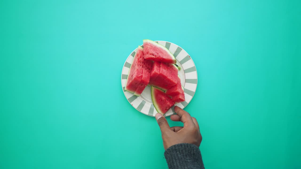 Person picking up a slice of watermelon from a plate