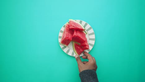 person picking up a slice of watermelon from a plate