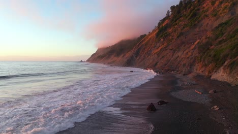 Northern California waves crashing bluffs cliffside mountain rocky rugged remote coast aerial drone vibrant sunset USAL Beach Campground Sinkyone Wilderness surf swell black sand forward slowly motion