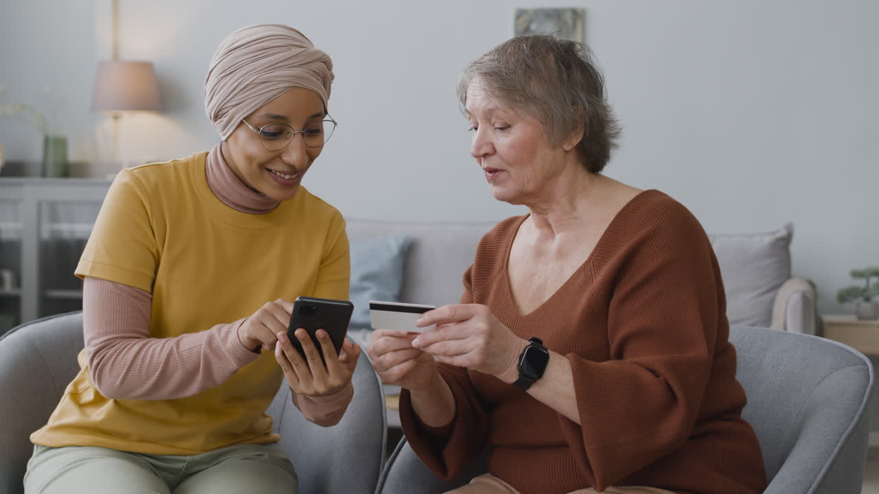 Arabic Woman Teaching An Elderly Woman To Use Mobile Payment With Credit Card