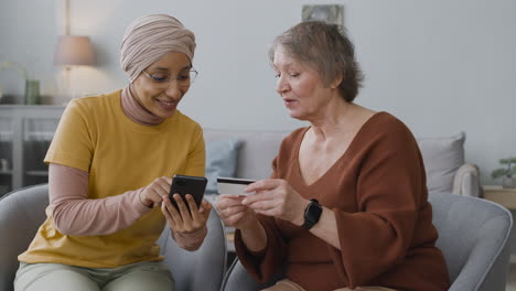 arabic woman teaching an elderly woman to use mobile payment with credit card