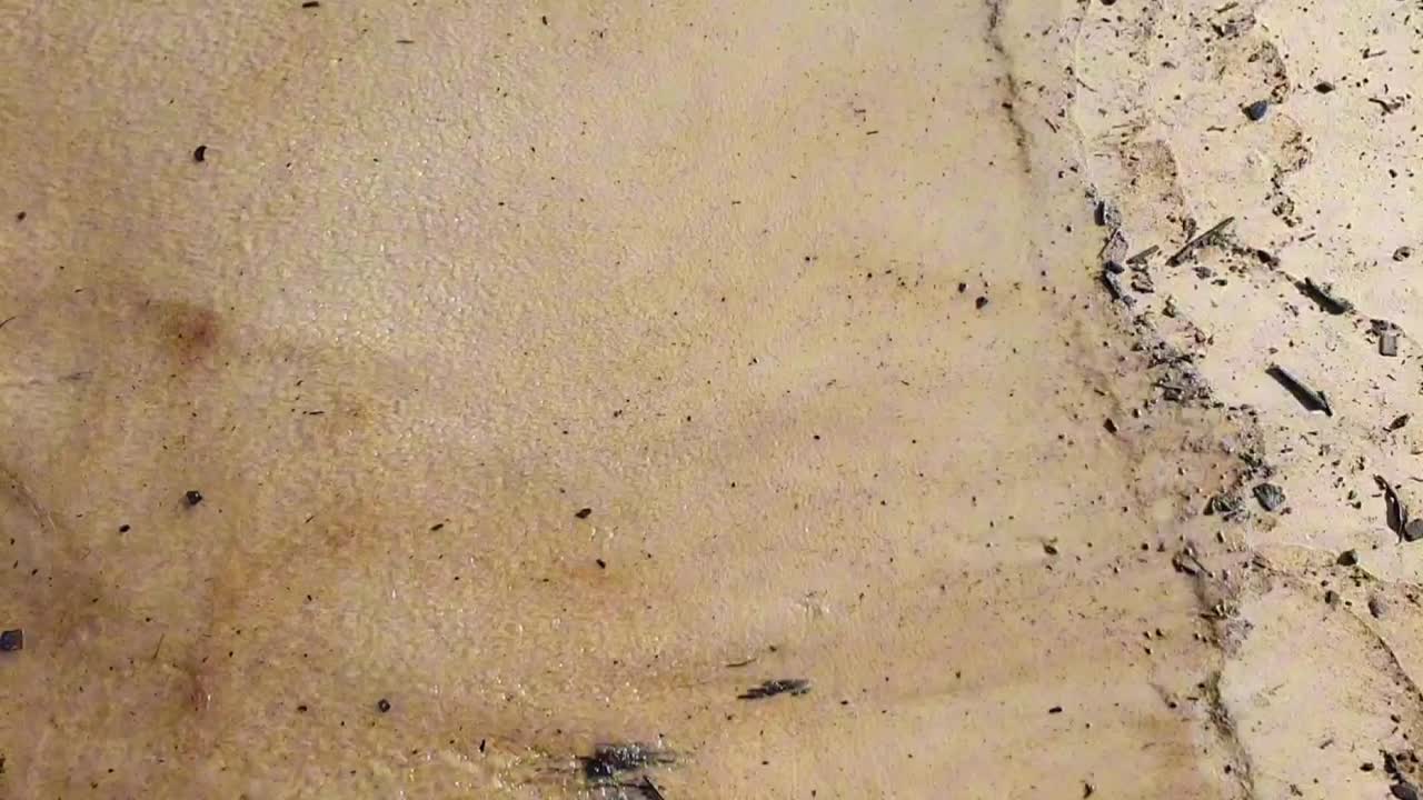 vista aérea de agua de mar sucia, empapada de petróleo negro golpeando la orilla con escombros en la arena