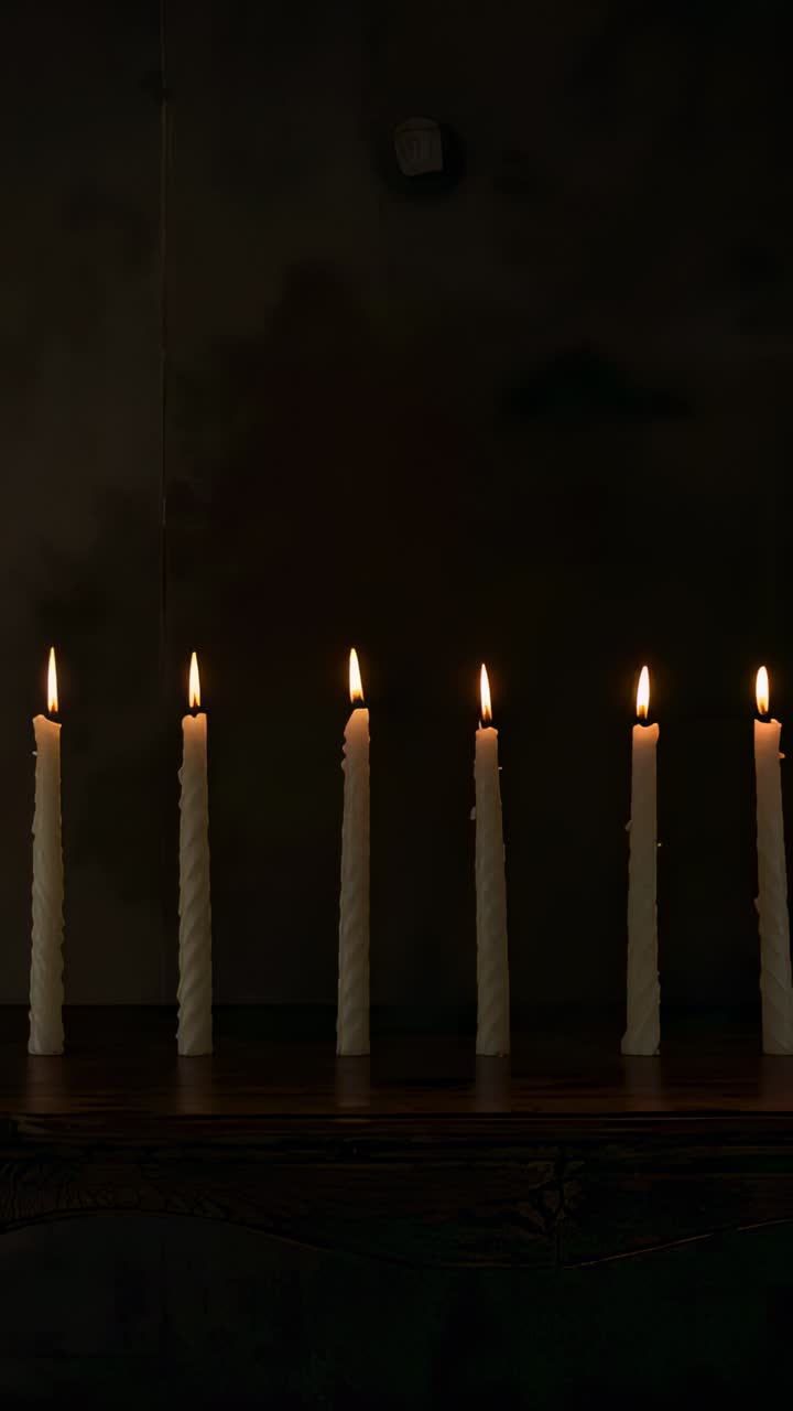 Video verticale: Sette candele bianche alte e tremolanti che si spengono lungo la mensola in legno, sensore sopra