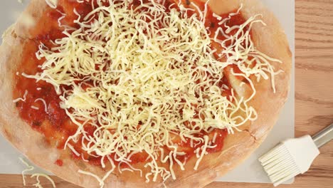 scattering grated cheese over pizza topping, wooden table bacground