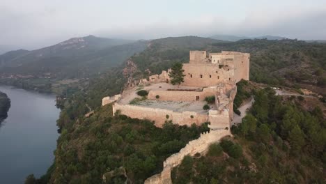 drone view of miravet castle and ebro river on foggy day