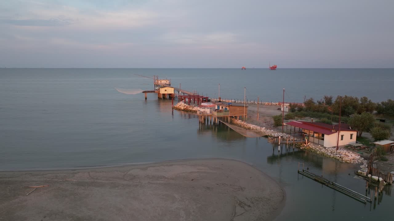 vista aérea en cámara lenta de cabañas de pesca a orillas del estuario al atardecer, máquina de pesca italiana, llamada "trabucco", lido di dante, ravenna cerca del valle de comacchio