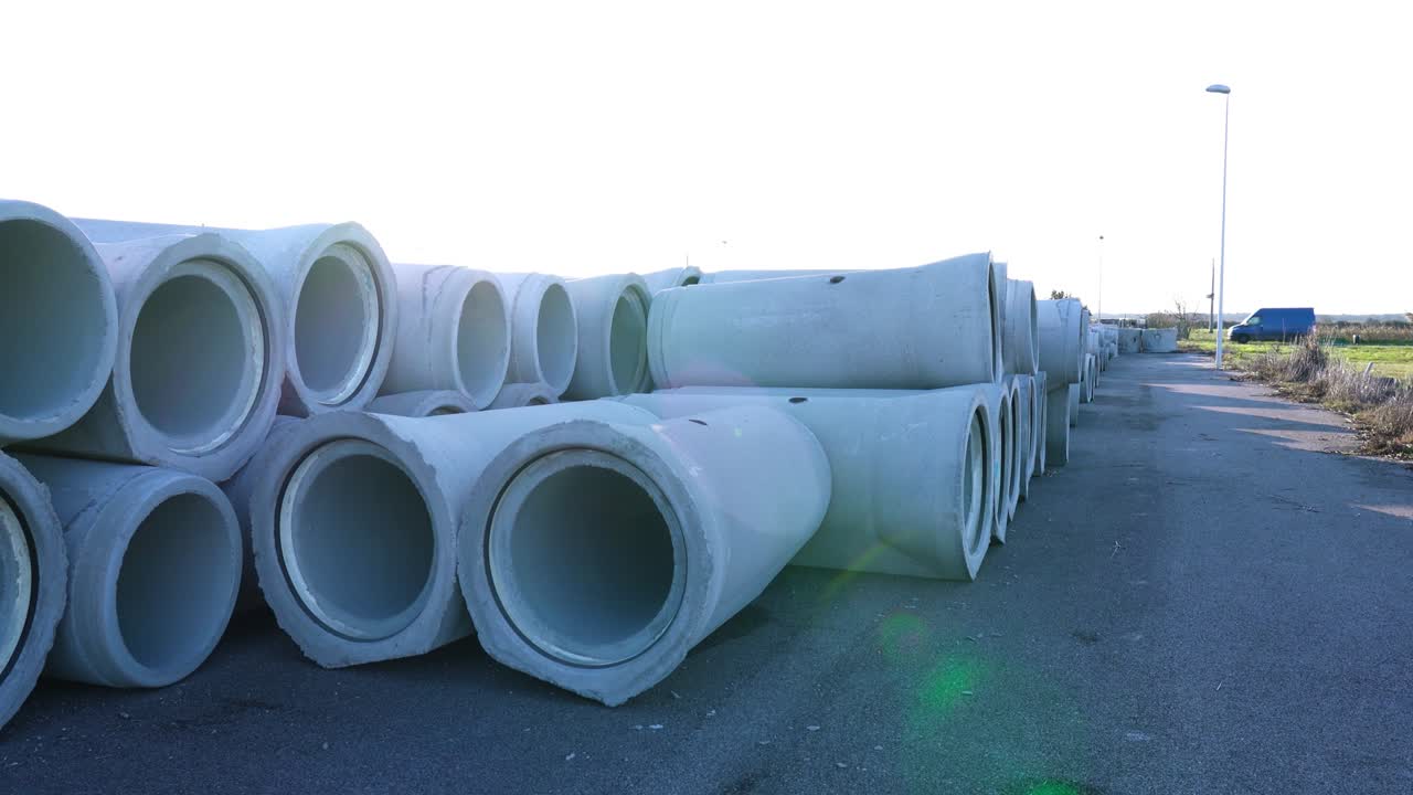 Pile of concrete pipes ready to install on asphalt ground