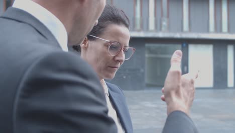 close up of two business partners discussing project using tablet while standing near office building outside