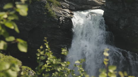 Hallingsafallet-waterfall-seen-behind-the-summer-foliage,-cascading-over-the-rocky-canyon