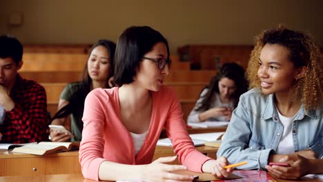 two friends students are talking and laughing during break between lessons at high school, african american girl is holding smartphone. communication and people concept.