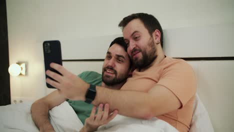 Una-Pareja-Gay-Se-Hace-Selfie,-Se-Toma-Una-Foto-En-La-Cama-Y-Se-Divierte-Juntos-En-El-Dormitorio-Por-La-Mañana