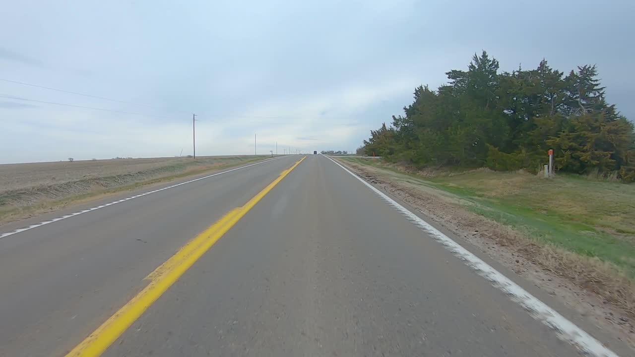 punto de vista conduciendo por un tramo recto de una carretera rural, pasando por un corral y campos cosechados