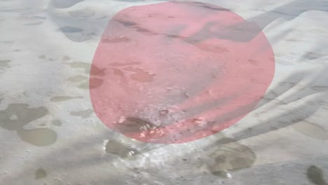 Digital-composition-japan-flag-waving-against-close-up-view-of-waves-on-the-beach