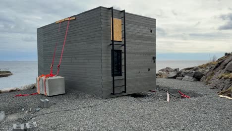 Storm-swept-holiday-hytter-into-the-sea,-Empty-foundation-and-secured-cabin-with-blocks,-handheld-panning-shot