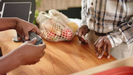 sección media de un hombre afroamericano de alto nivel pagando con tarjeta de crédito en una tienda de alimentos saludables, cámara lenta