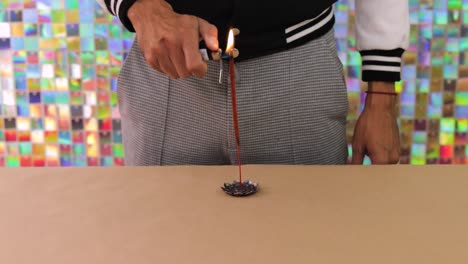 person lighting flower-shaped incense on table with colorful backdrop in close-up shot