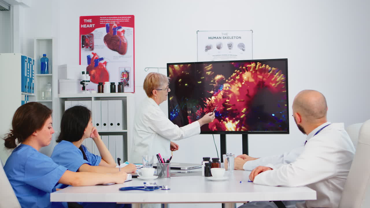 Medico senior che indica un monitor nell'ufficio dell'ospedale spiegando lo sviluppo del virus