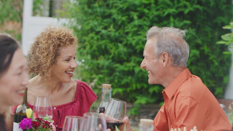 Group-Of-Mature-Friends-Talking-And-Drinking-Wine-At-Summer-Drinks-Party-In-Garden-At-Home
