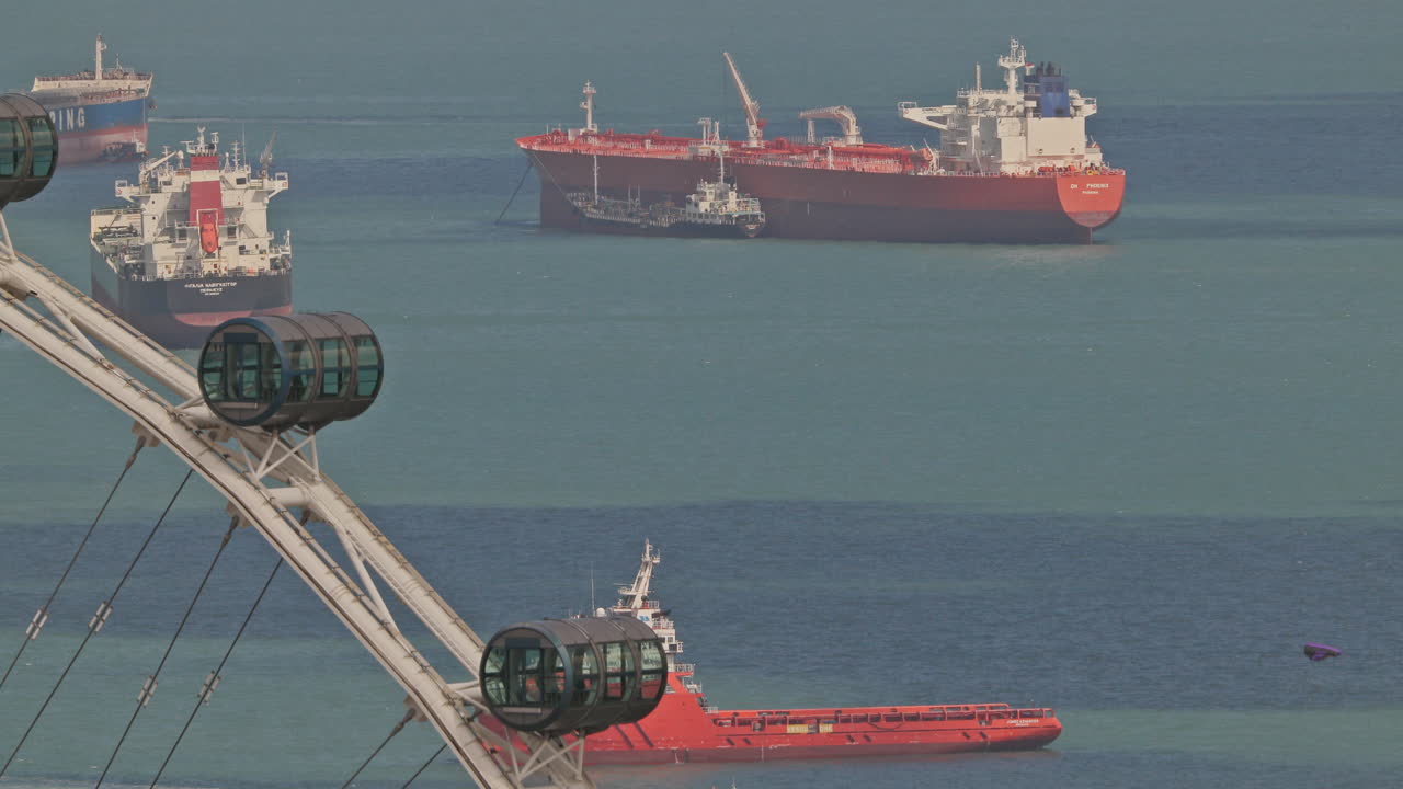 SINGAPORE - 5 MARCH 2025 : container ships waiting in the sea by singapore with observation ferris wheel in foreground