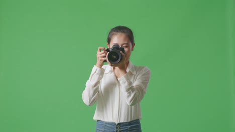 asian photographer telling the model to move left and right while taking pictures by camera on green screen background in the studio