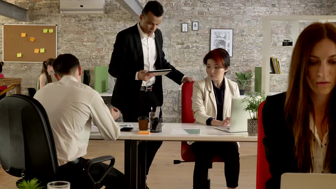 gente de negocios de raza mixta trabajando en la oficina, hombre negro viniendo a la mujer asiática y hablando por la tableta, hombre dando a la mujer documentos