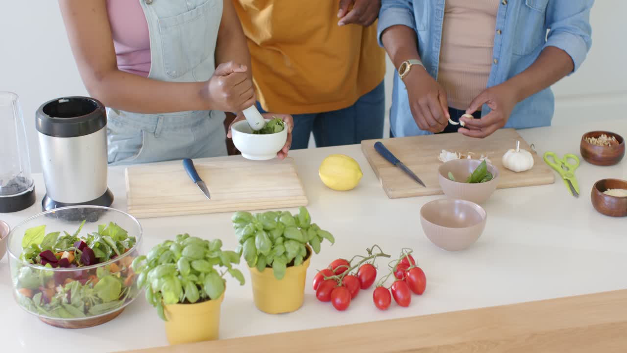 African family starting prep, muddling basil in mortar, peeling garlic at kitchen island for salad