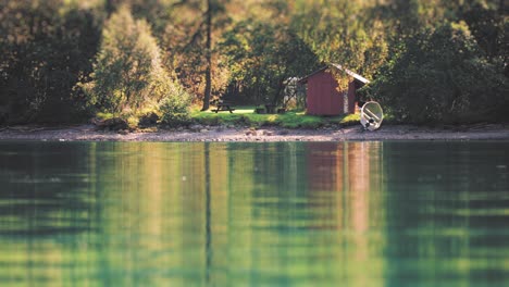 a small wooden cabin on the forest-covered shore of the lake