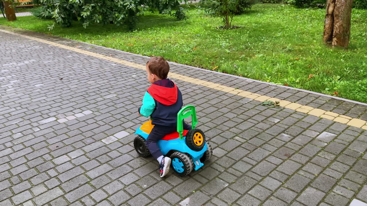 Cute smiling baby boy riding his colorful toy car. Little child having fun in the beautiful park.