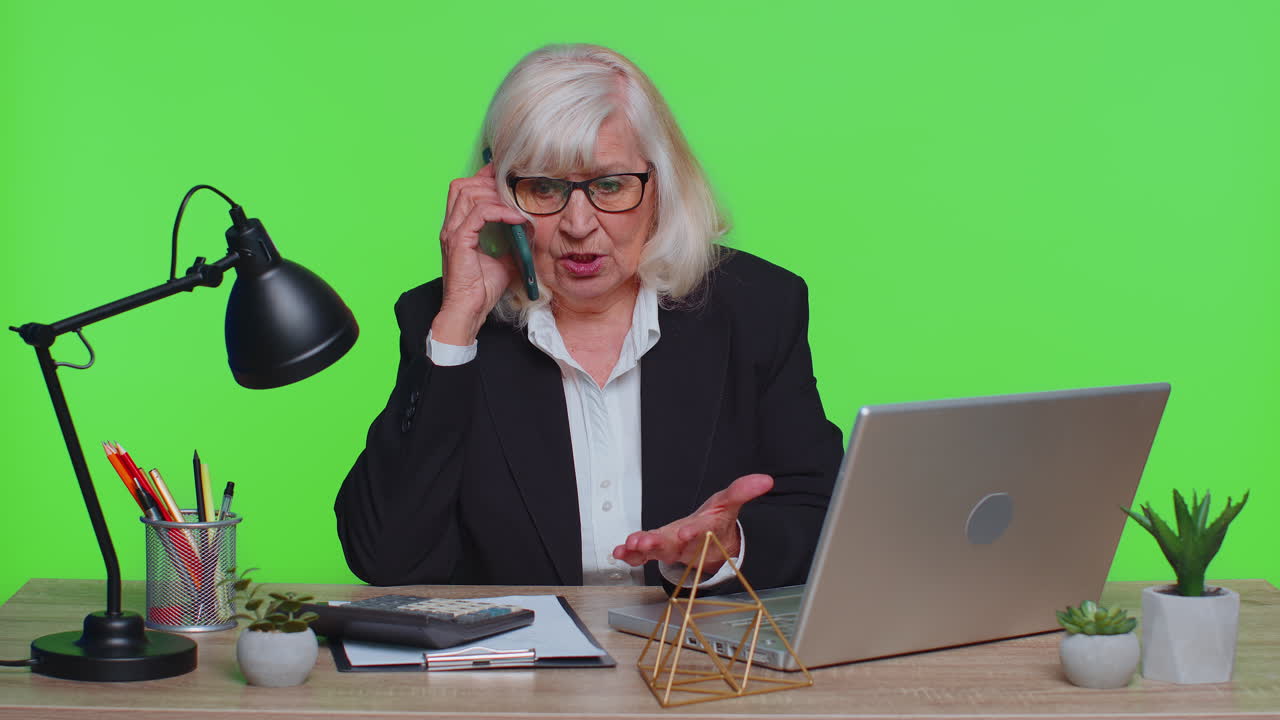 Angry senior old business woman making phone call at office work annoyed boss talking mobile quarrel