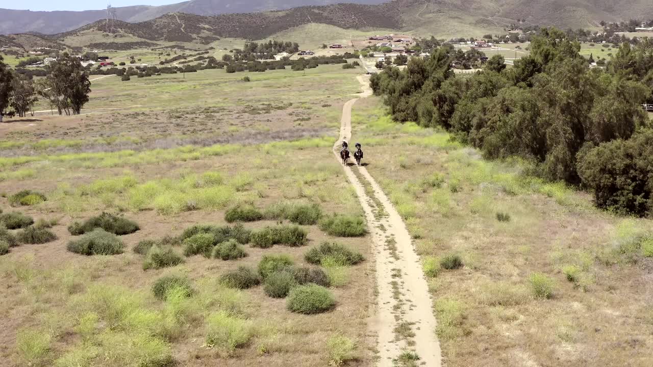 Two horse riders on horseback walking along country track, aerial follow