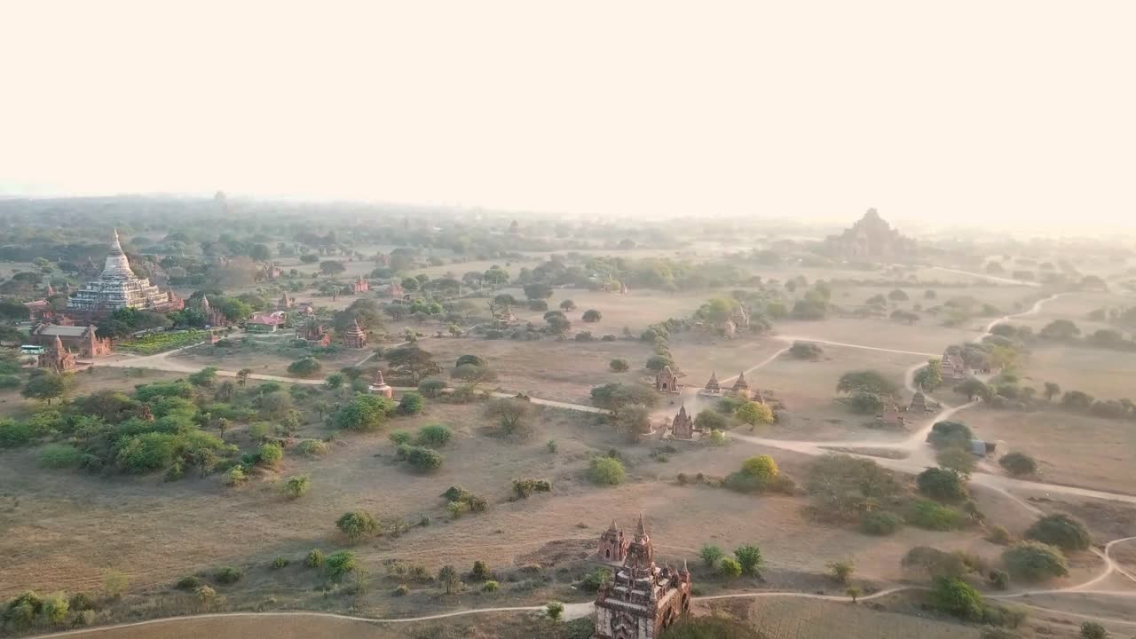 The vast plains of Bagan, Myanmar feature ancient temples and pagodas spread across dry, golden fields under a soft sunrise, evoking a timeless and spiritual atmosphere.