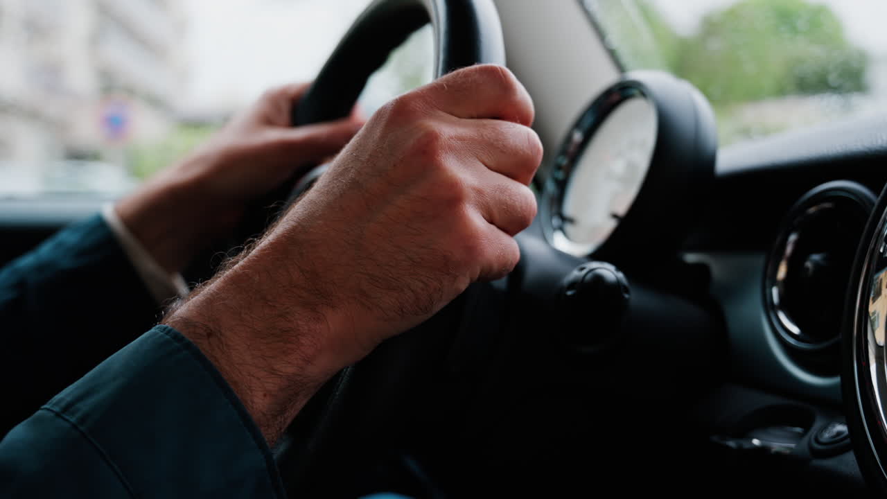 Close up of a man's hands on a steering wheel, driving a car on the road in the rain