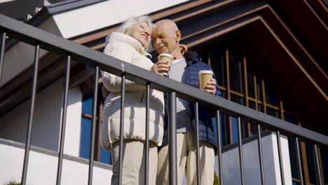 Senior couple hugging while holding coffees to go on a terrace in the park on a winter day