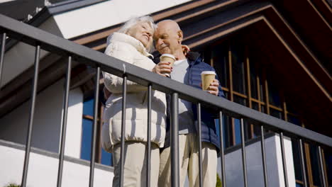 senior couple hugging while holding coffees to go on a terrace in the park on a winter day