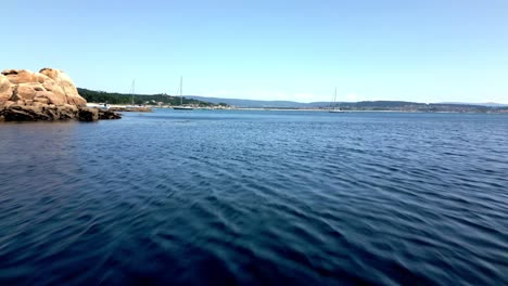 Aerial-Drone-Footage-Clear-and-Dark-Water-Rocky-Shore-Sailboats-Wooded-Horizon