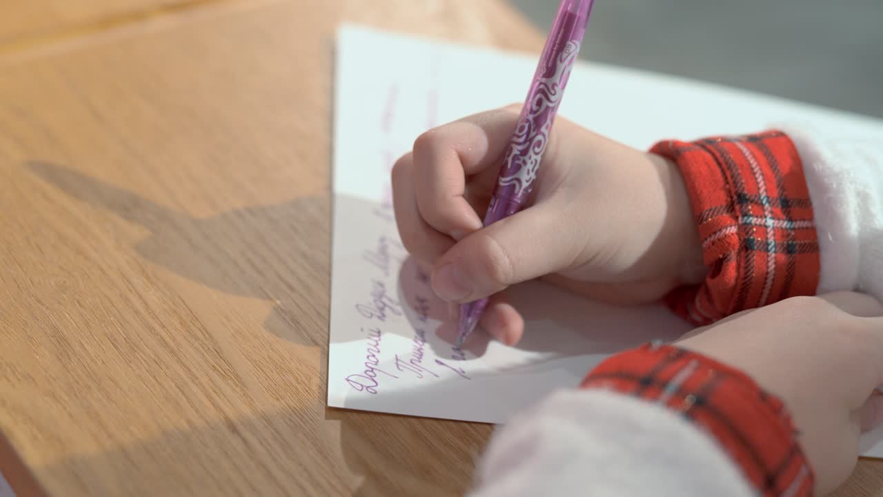 Close-up of children's hands. The girl writes a letter with a pen on paper in Ukrainian