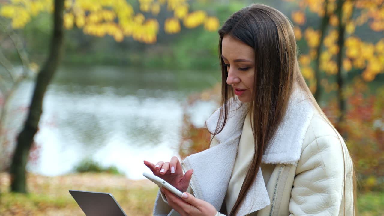 Woman using tablet and laptop in autumn park by the lake