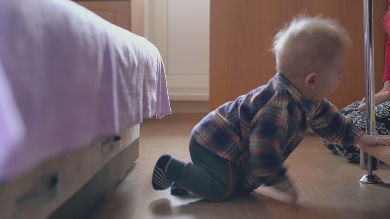 el bebé se arrastra al estante cerca de la madre joven en la habitación de los niños