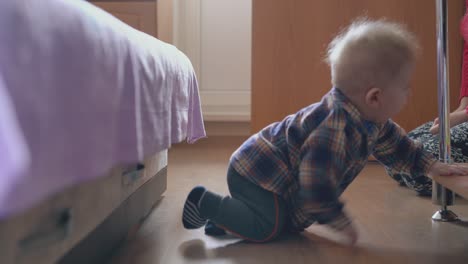 baby crawls to rack near young mother in children room