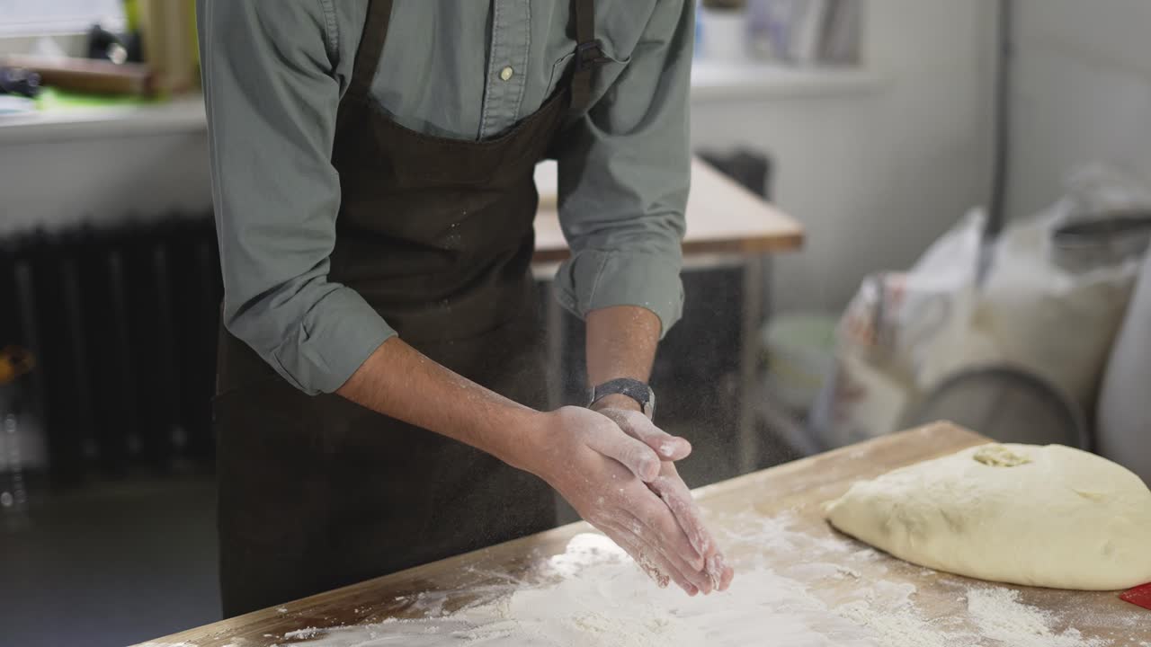 Unrecognizable male baker claps and scatters white flour in the air. Young man making homemade bread claps with a handful of organic whole wheat flour in each hand. Slow motion, close up