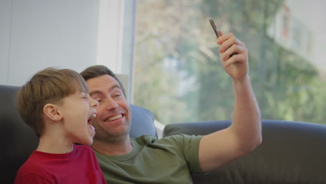 Padre-Con-Hijo-En-Pijama-Sentado-En-Un-Sofá-Posando-Para-Selfie-En-Teléfono-Móvil---Filmado-En-Cámara-Lenta